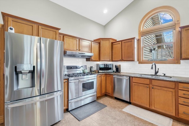 kitchen with under cabinet range hood, appliances with stainless steel finishes, brown cabinetry, and a sink