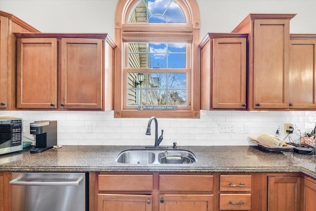 kitchen featuring dark stone counters, decorative backsplash, appliances with stainless steel finishes, brown cabinetry, and a sink