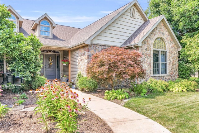 view of front of home featuring a front yard, stone siding, and roof with shingles