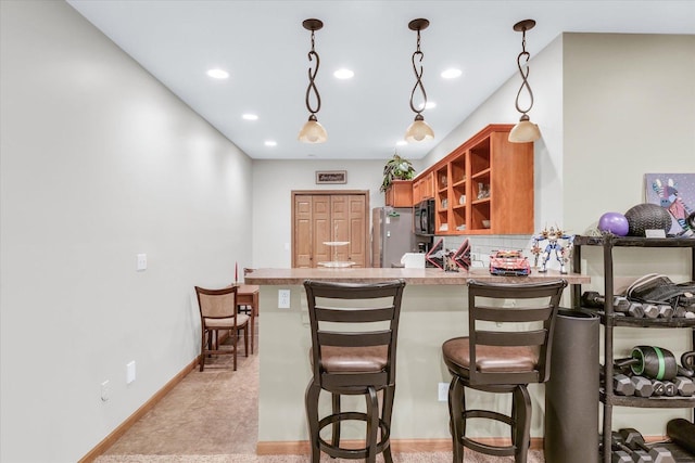 kitchen with black microwave, a breakfast bar, brown cabinets, a peninsula, and freestanding refrigerator