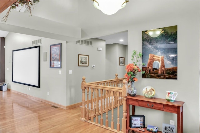 corridor with wood finished floors, an upstairs landing, visible vents, and baseboards