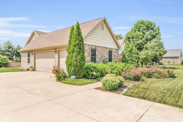 view of home's exterior with driveway, roof with shingles, a yard, an attached garage, and stone siding