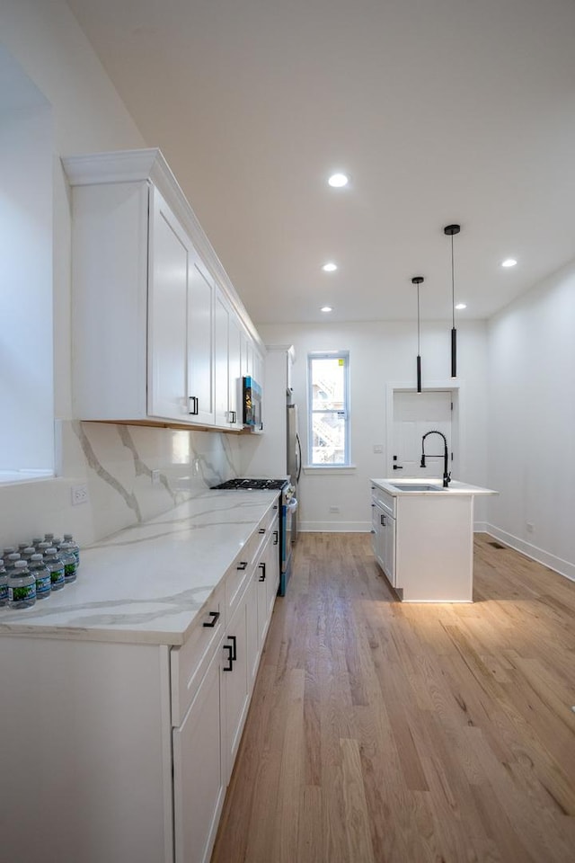 kitchen with light wood-type flooring, a center island with sink, white cabinetry, stainless steel appliances, and decorative backsplash