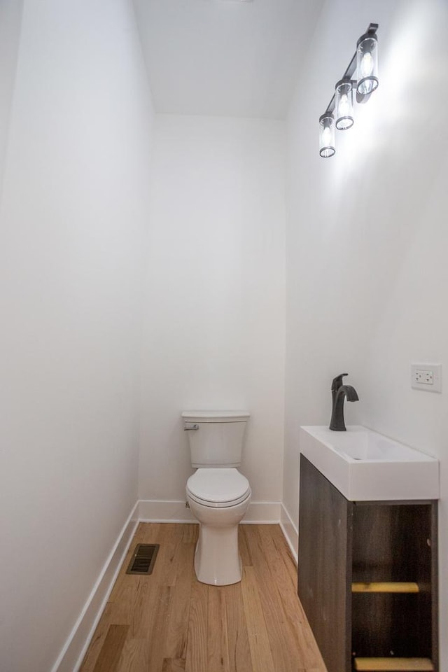 half bath featuring visible vents, baseboards, toilet, wood finished floors, and vanity