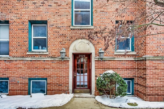 snow covered property entrance featuring brick siding