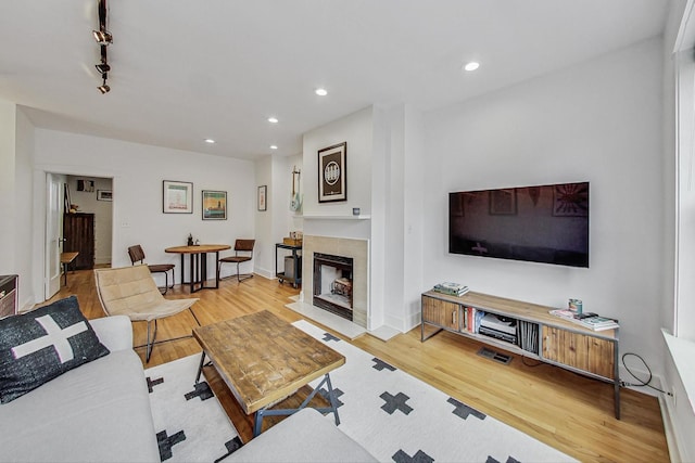 living area featuring a tiled fireplace, track lighting, recessed lighting, and wood finished floors