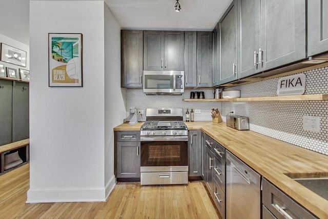 kitchen featuring backsplash, butcher block counters, light wood-style flooring, appliances with stainless steel finishes, and open shelves