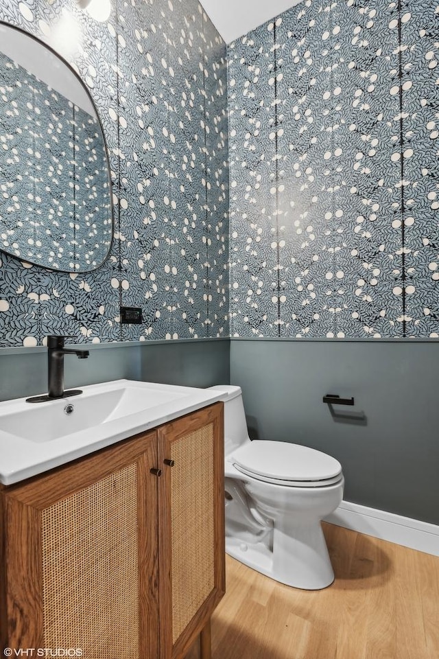 half bath with toilet, wood finished floors, and vanity