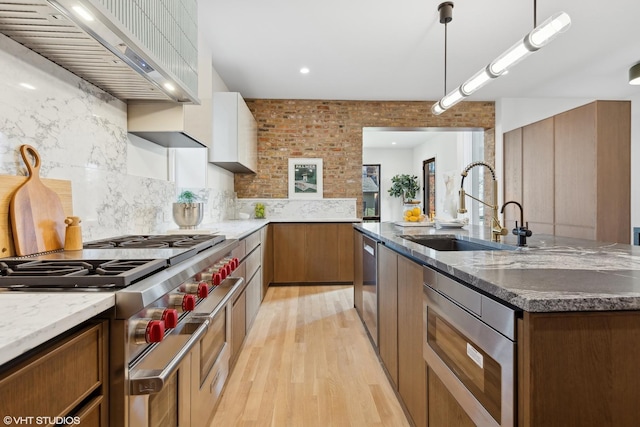 kitchen with backsplash, wall chimney range hood, light wood-style flooring, stainless steel appliances, and a sink