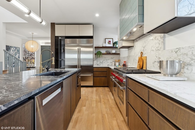 kitchen featuring light wood-style flooring, a sink, premium appliances, open shelves, and dark stone counters