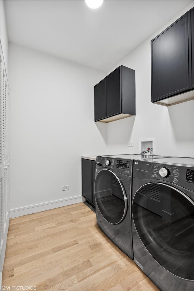 washroom with cabinet space, baseboards, light wood finished floors, and washing machine and clothes dryer