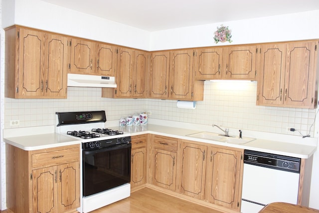 kitchen featuring white dishwasher, a sink, under cabinet range hood, range with gas cooktop, and backsplash