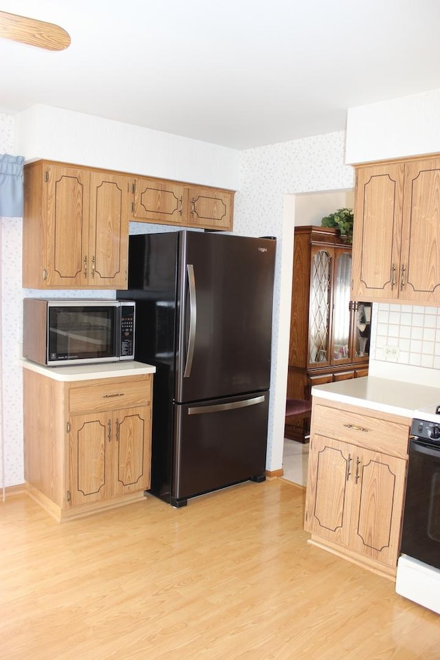 kitchen featuring light wood-type flooring, freestanding refrigerator, wallpapered walls, range, and light countertops