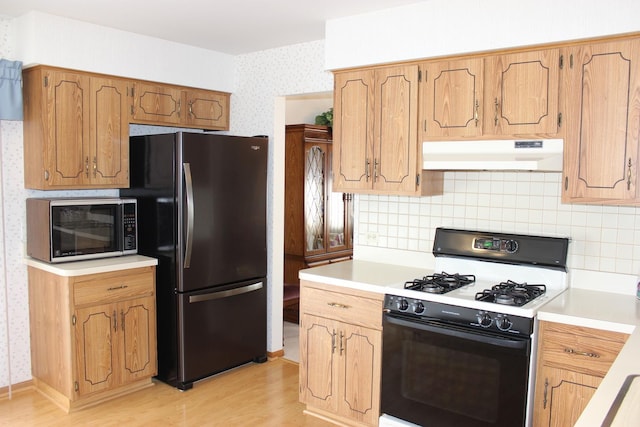 kitchen featuring range with gas stovetop, wallpapered walls, freestanding refrigerator, light countertops, and under cabinet range hood