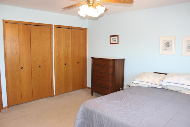 bedroom with ceiling fan, multiple closets, and light carpet