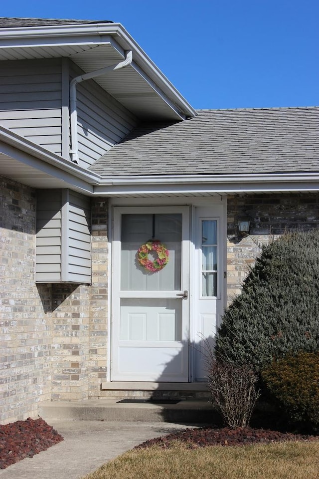 property entrance featuring brick siding and roof with shingles