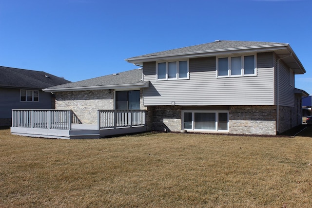 back of property featuring brick siding, a wooden deck, a lawn, and a shingled roof