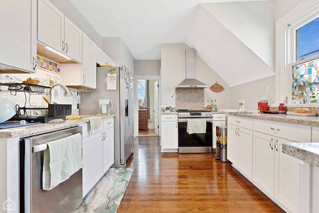 kitchen with vaulted ceiling, appliances with stainless steel finishes, wood finished floors, white cabinets, and wall chimney exhaust hood