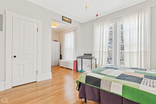 bedroom featuring light wood-style flooring, radiator heating unit, and ornamental molding