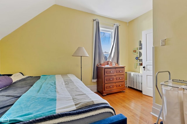 bedroom with vaulted ceiling, light wood-style flooring, radiator, and baseboards