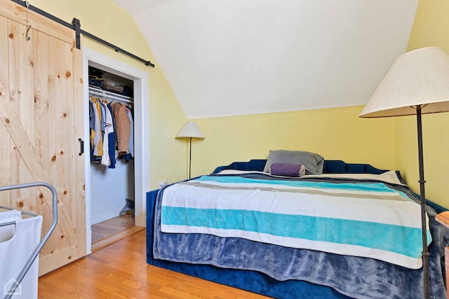 bedroom featuring a closet, vaulted ceiling, a barn door, and wood finished floors