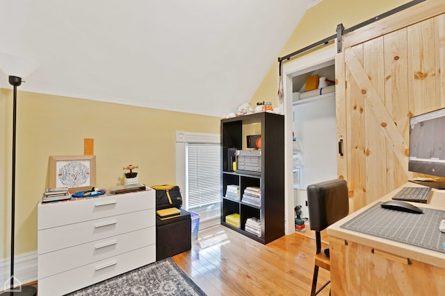 office with light wood-type flooring, a barn door, and vaulted ceiling