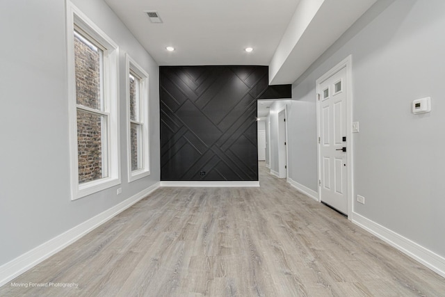 spare room with visible vents, light wood-type flooring, an accent wall, and baseboards