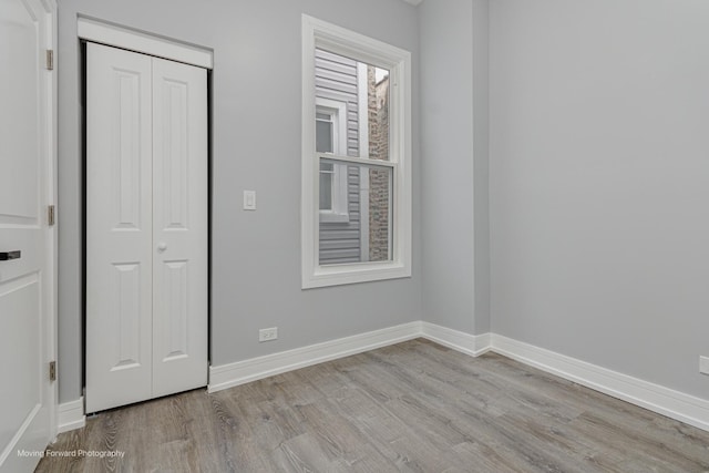 unfurnished bedroom featuring wood finished floors, baseboards, and a closet