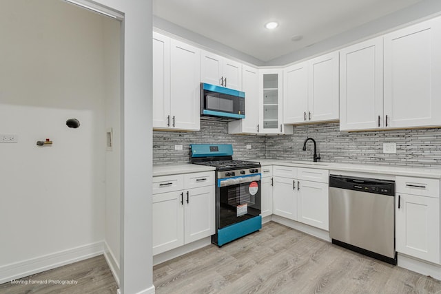 kitchen with a sink, tasteful backsplash, stainless steel appliances, light wood finished floors, and light countertops