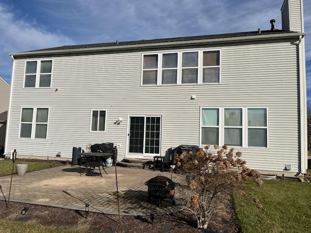 rear view of property featuring a patio area, a fire pit, a chimney, and a lawn