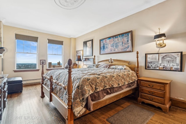 bedroom with a baseboard heating unit, hardwood / wood-style floors, and ornamental molding