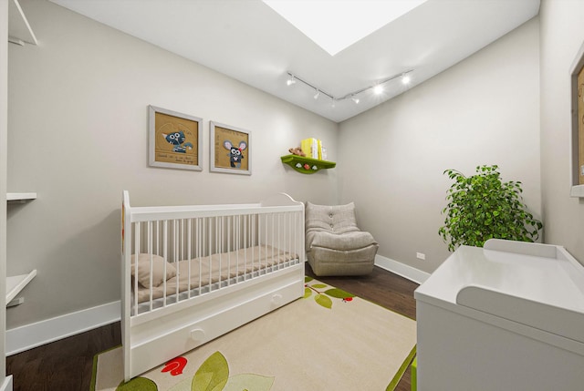 bedroom featuring a crib, wood finished floors, a skylight, rail lighting, and baseboards