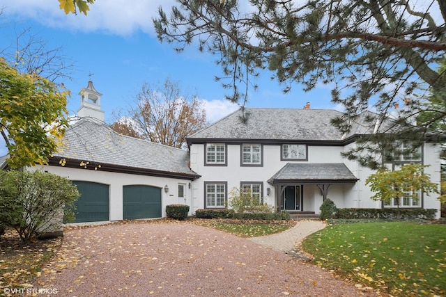 view of front facade with a front lawn, aphalt driveway, a high end roof, a chimney, and an attached garage