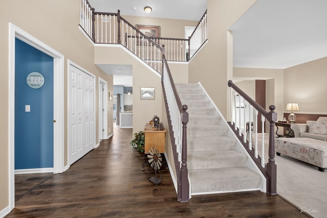 staircase featuring wood finished floors, baseboards, and a towering ceiling