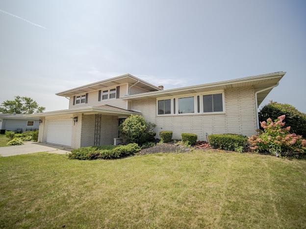 split level home featuring brick siding, an attached garage, concrete driveway, and a front yard