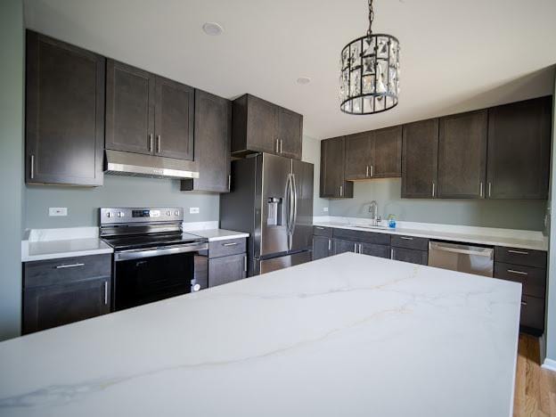 kitchen featuring under cabinet range hood, a sink, stainless steel appliances, dark brown cabinetry, and hanging light fixtures