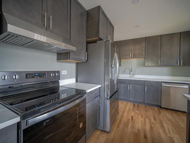 kitchen featuring a sink, under cabinet range hood, stainless steel appliances, light wood-style floors, and light countertops