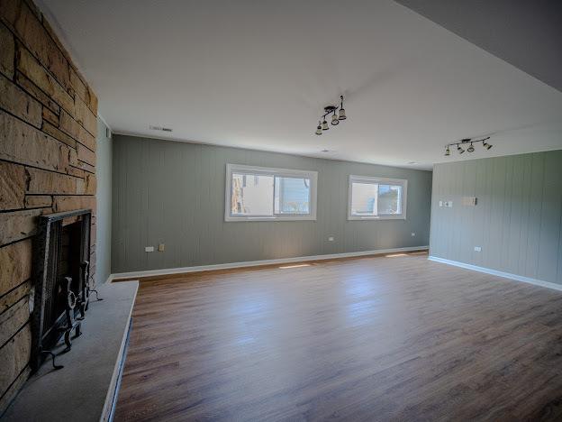 unfurnished living room featuring track lighting, a large fireplace, baseboards, and wood finished floors