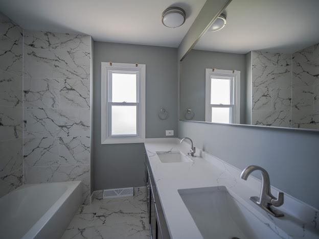 bathroom with double vanity, marble finish floor, a tub, and a sink