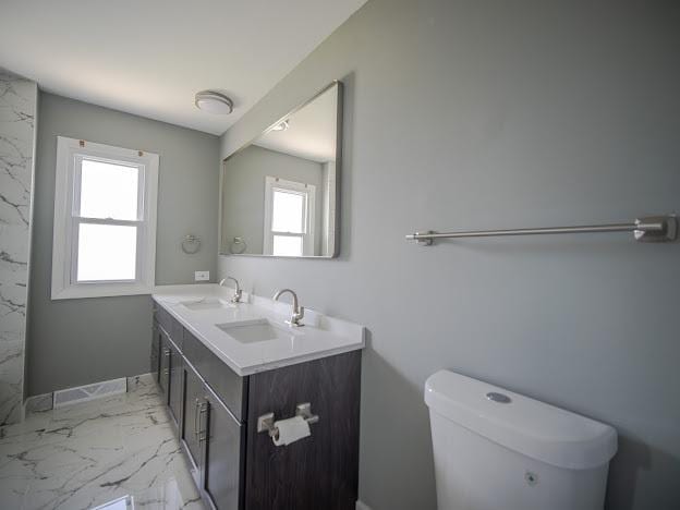 bathroom with double vanity, toilet, marble finish floor, and a sink