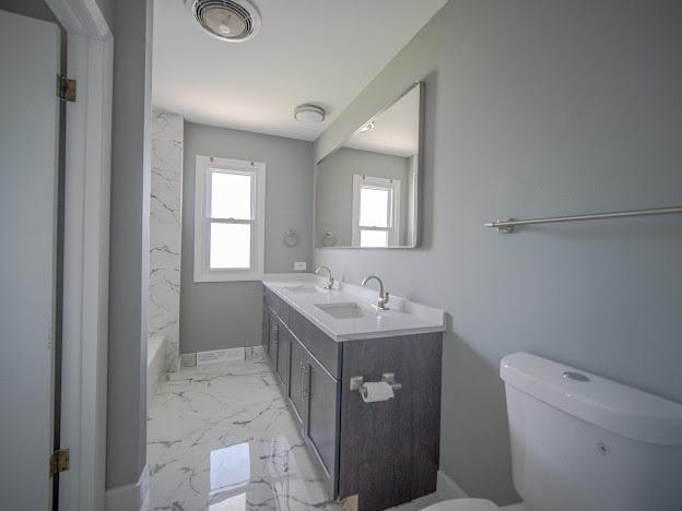 bathroom featuring a bath, marble finish floor, toilet, and a sink