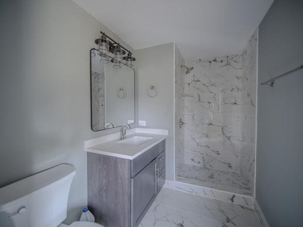 bathroom with tiled shower, toilet, marble finish floor, and vanity