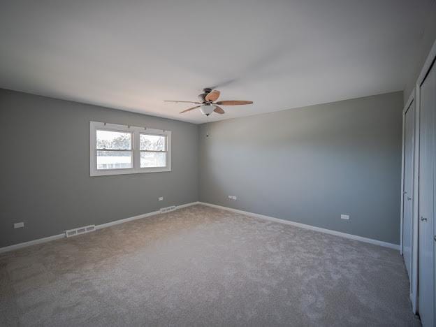 empty room featuring a ceiling fan, carpet flooring, visible vents, and baseboards