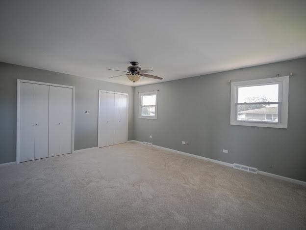 unfurnished bedroom with light colored carpet, visible vents, multiple closets, and a ceiling fan