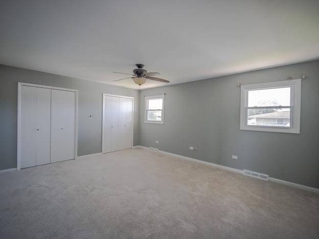 unfurnished bedroom with visible vents, baseboards, multiple closets, light colored carpet, and a ceiling fan