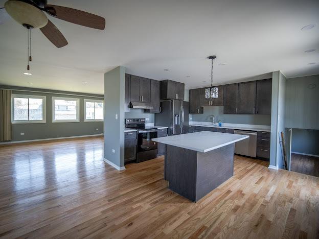 kitchen featuring under cabinet range hood, open floor plan, light countertops, light wood-style floors, and stainless steel appliances