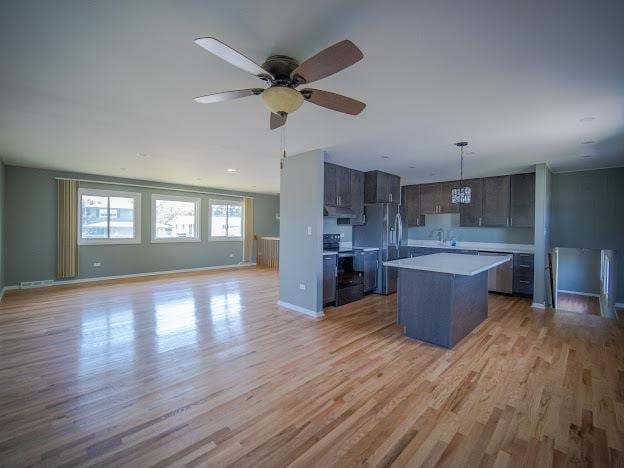 kitchen featuring light wood-style flooring, a kitchen island, open floor plan, appliances with stainless steel finishes, and light countertops