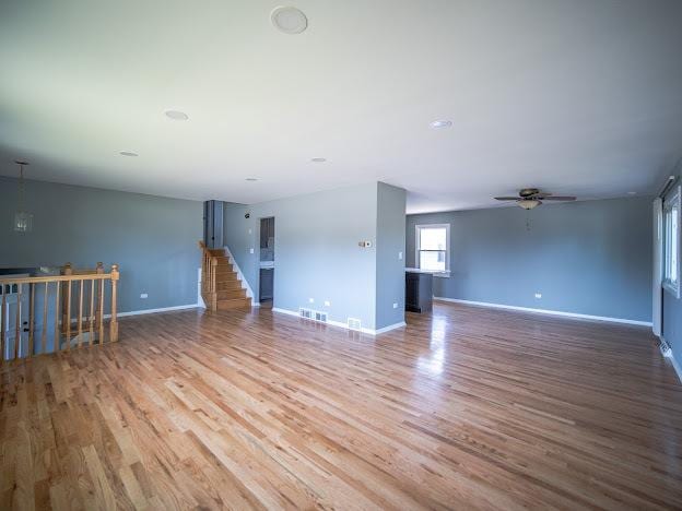 unfurnished living room featuring visible vents, stairway, baseboards, and wood finished floors