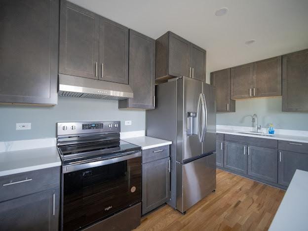 kitchen with stainless steel fridge with ice dispenser, under cabinet range hood, light countertops, range with electric stovetop, and a sink