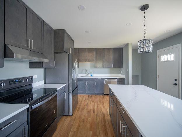 kitchen featuring under cabinet range hood, light wood-type flooring, electric stove, hanging light fixtures, and stainless steel dishwasher